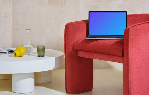 MacBook mockup at the edge of a red chair with a center table at the side