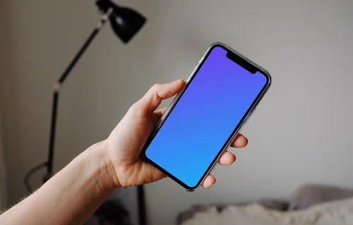 iPhone 12 Pro mockup tenu par un utilisateur avec une lampe de lecture en arrière-plan.