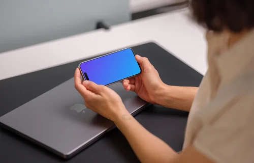 iPhone 15 Pro mockup in a woman's hand over a laptop