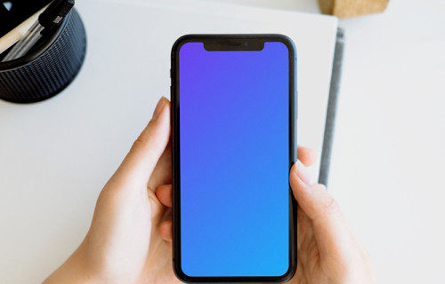 iPhone mockup held with two hands by a user above a white table