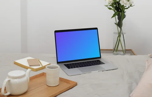 MacBook mockup sobre una cama con un jarrón de flores al fondo