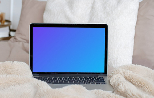 MacBook mockup on a cream-colored bed with white pillows in the background