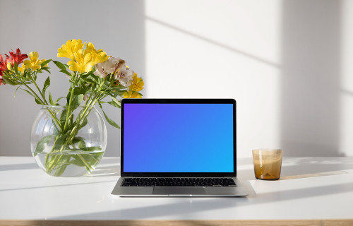 MacBook mockup sobre una mesa con un jarrón de flores que contiene agua y hermosas flores