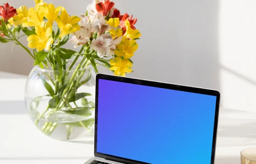 MacBook mockup on a white table beside a bowl-shaped flower vase close