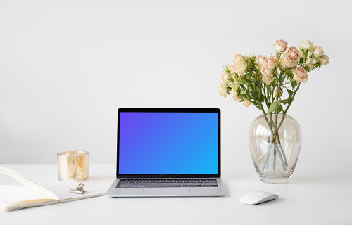 MacBook mockup on a white table with a wireless mouse and a vase of rose
