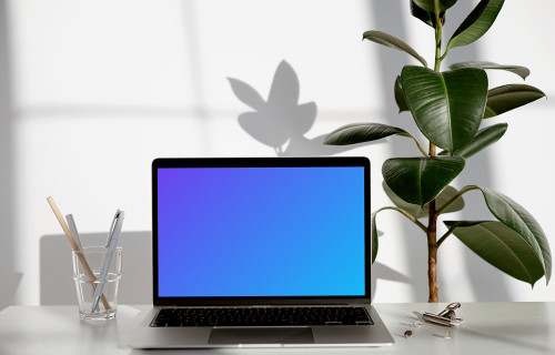 MacBook mockup sur une table blanche avec une plante à racine dure sur le côté