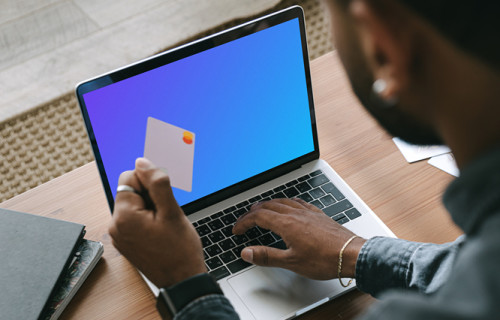 Man in grey shirt shopping mockup paying online with Mastercard on grey MacBook 