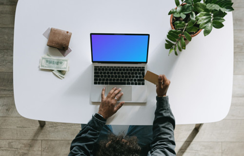 Mockup of man paying for an item on a grey MacBook beside a wallet.