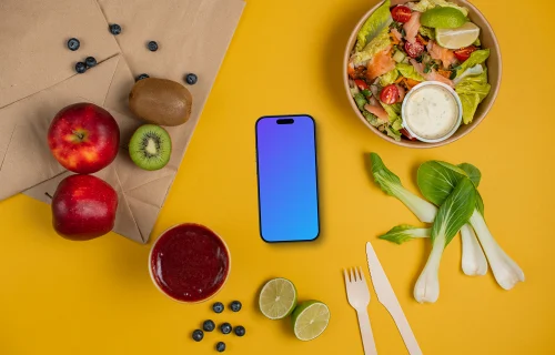 Smartphone mockup between fresh fruits and salad