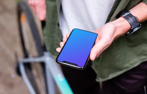 Holding an iPhone 11 Pro mockup whilst stood with a bike