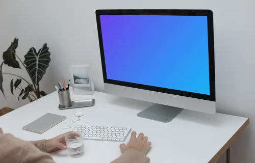 iMac on a white table with a cup of water