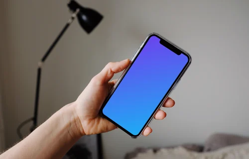 iPhone 12 Pro mockup held by user with a reading lamp in the background