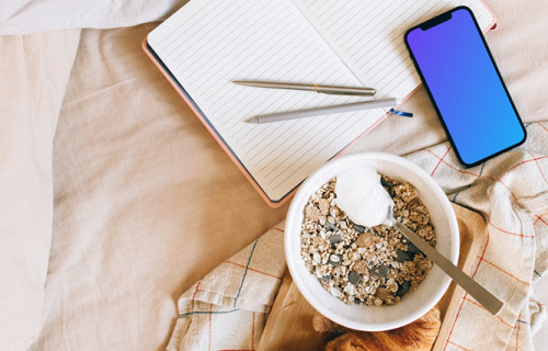 iPhone 12 Pro mockup on a bed, with a tray of food at its side