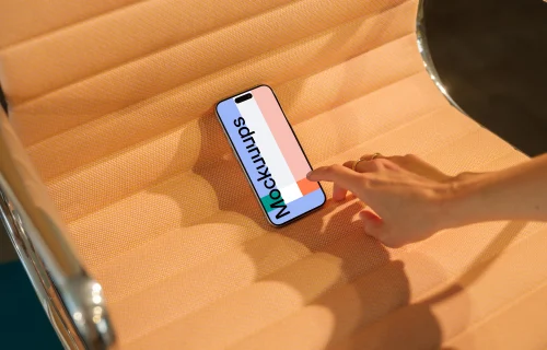 mockup iPhone 15 Pro sur un siège orange texturé avec une main en interaction