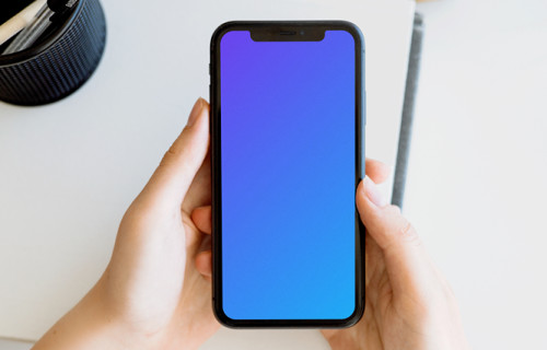 iPhone mockup held with two hands by a user above a white table