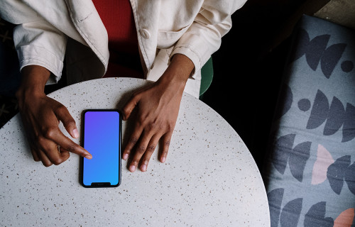 iPhone mockup on white table and a bed by the side