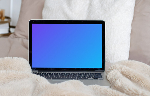 MacBook mockup on a cream-colored bed with white pillows in the background