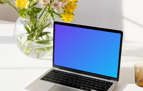 MacBook mockup on a white table beside a bowl-shaped flower vase close