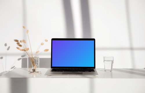 MacBook mockup on a white table with glass of water next to it
