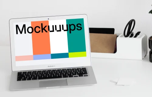 MacBook mockup on a white table with writing materials on the side