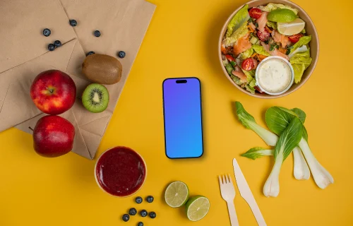 Smartphone mockup between fresh fruits and salad