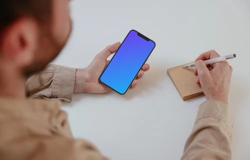 User holding an iPhone and writing into a sticky note mockup