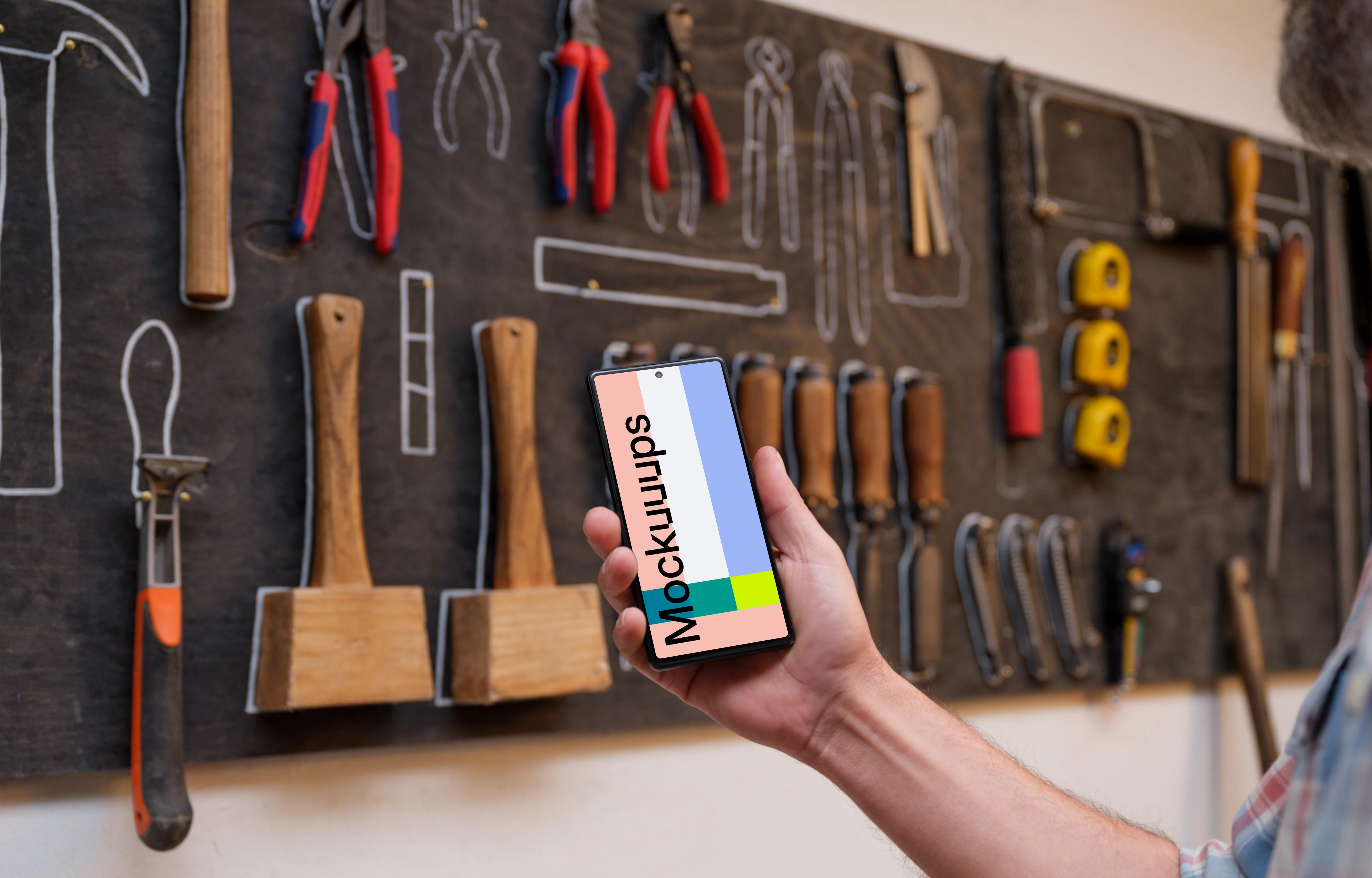 Mechanic holding a phone in front of a wall with tools