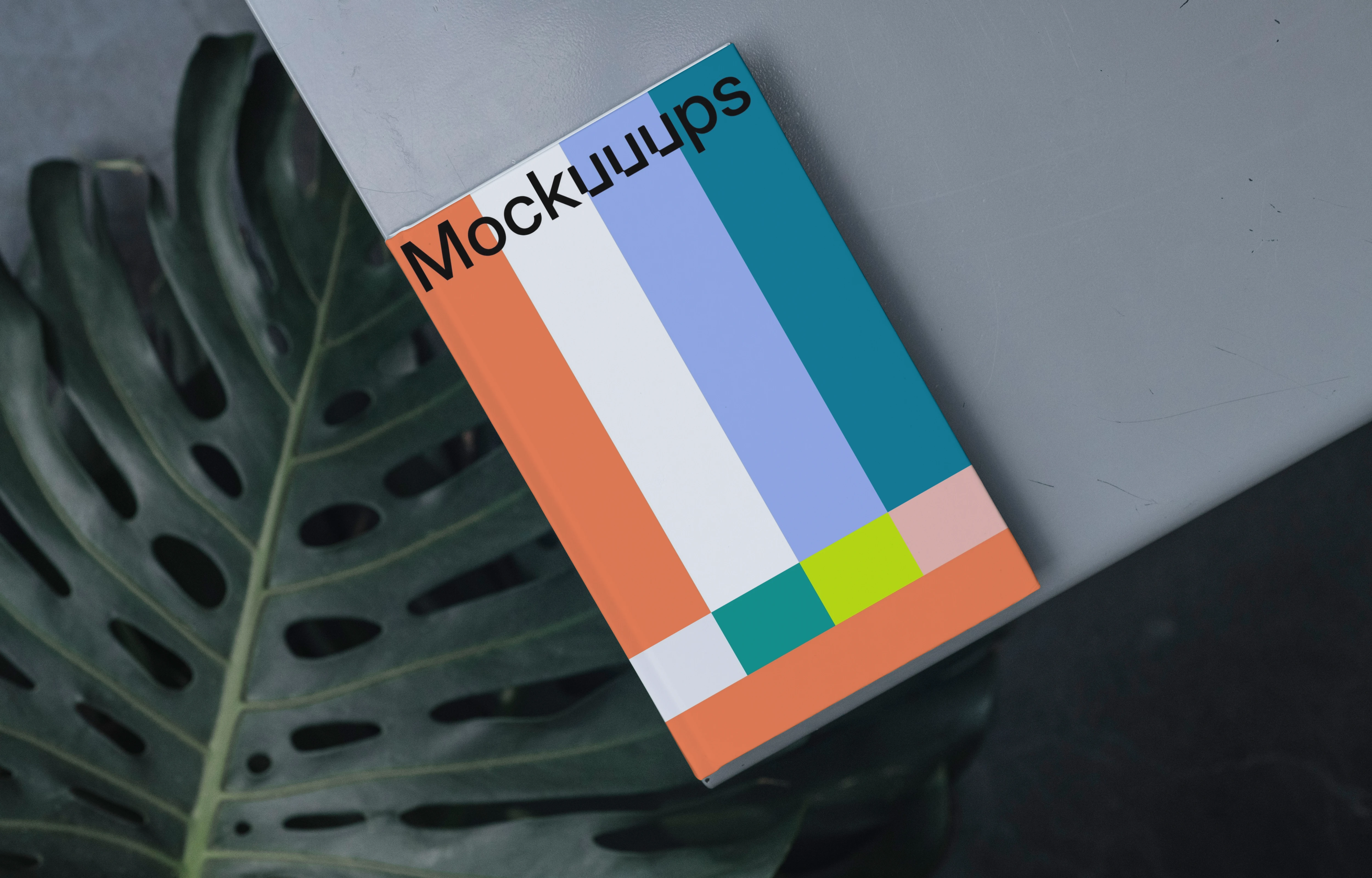 C-format book mockup on a gray surface with a tropical leaf