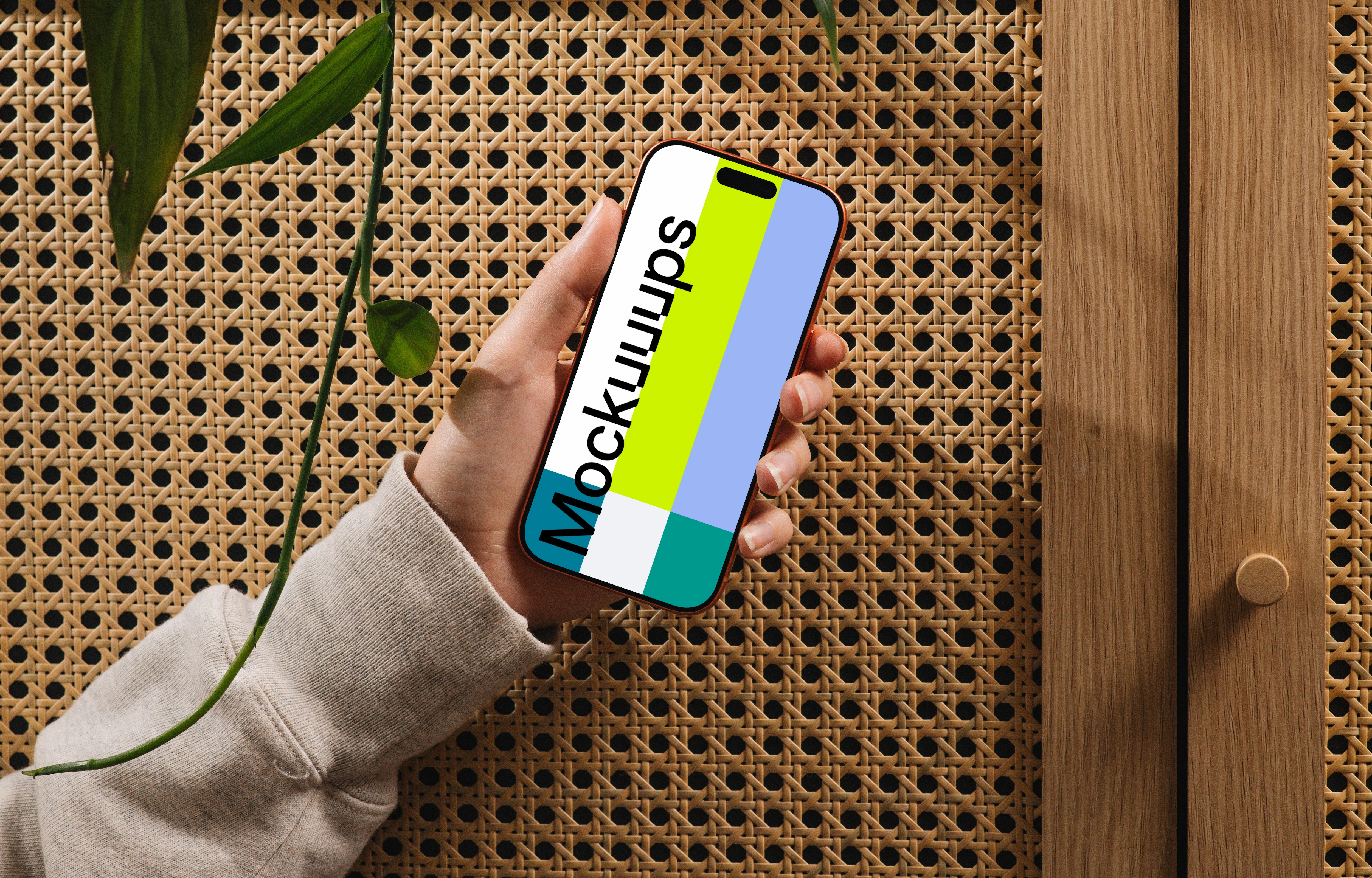 Hand holding iPhone 17 Pro mockup against a woven wood backdrop