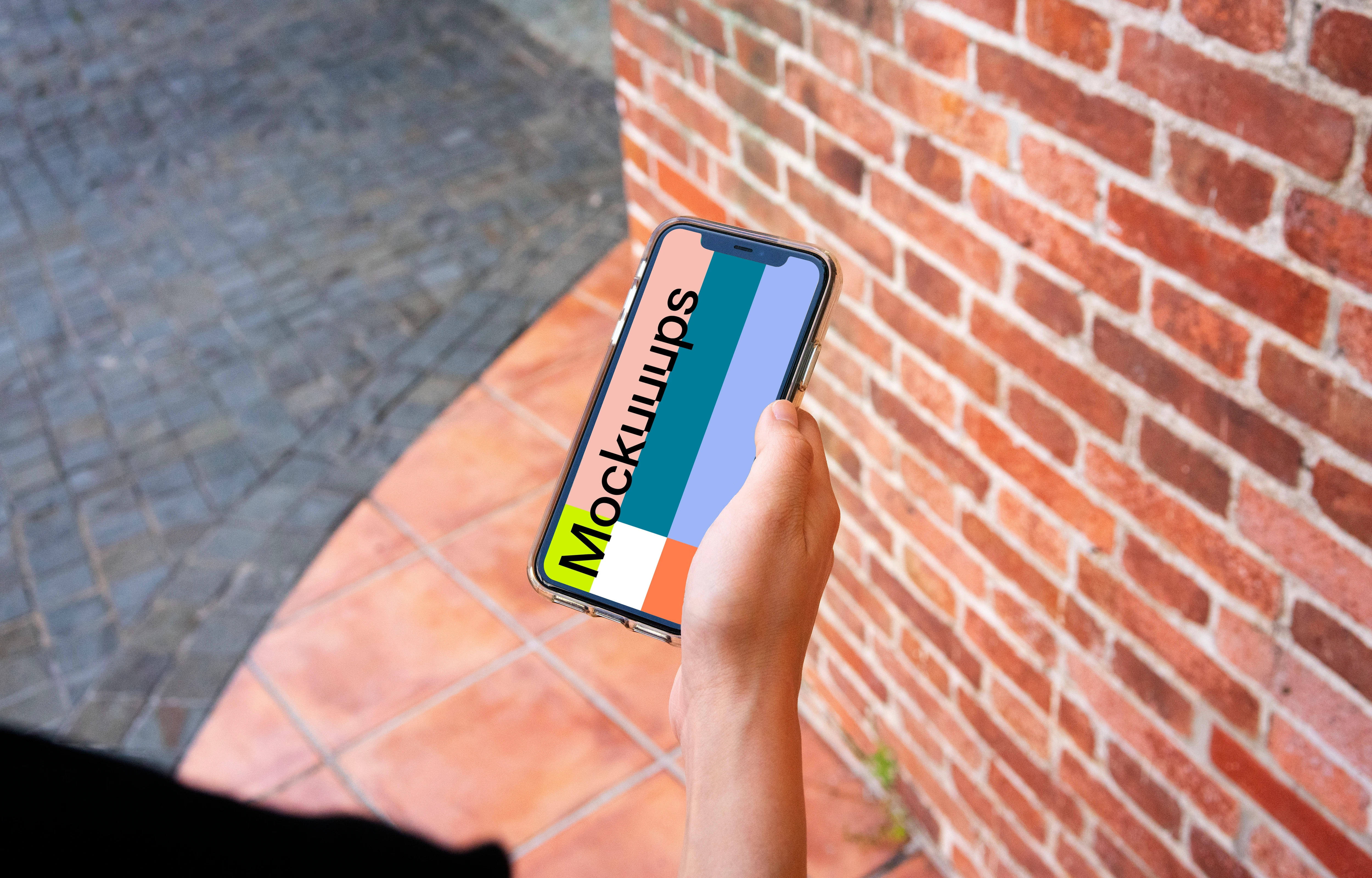 iPhone mockup held beside a brick wall