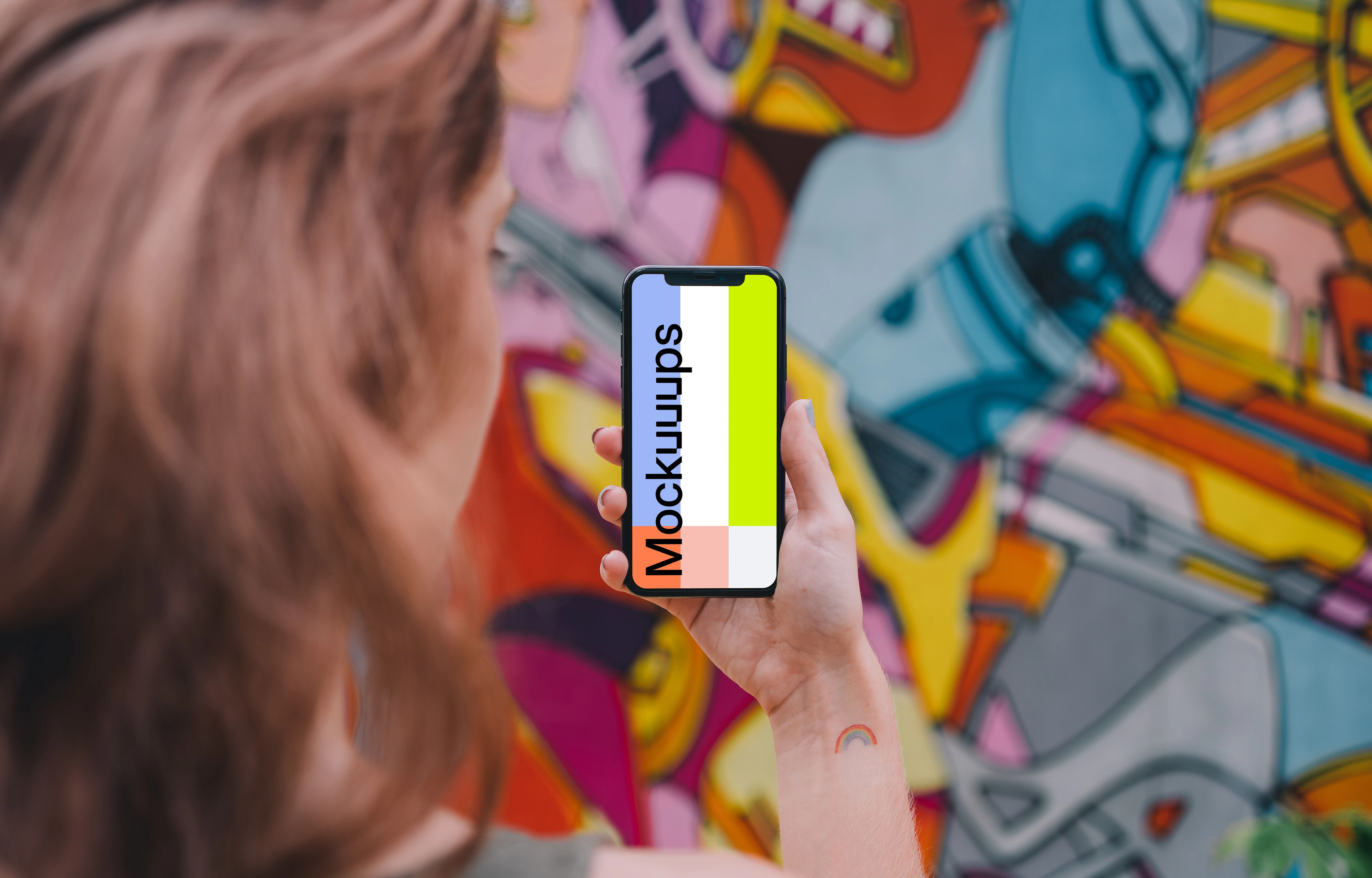 User holding iPhone in front of graffiti wall mockup