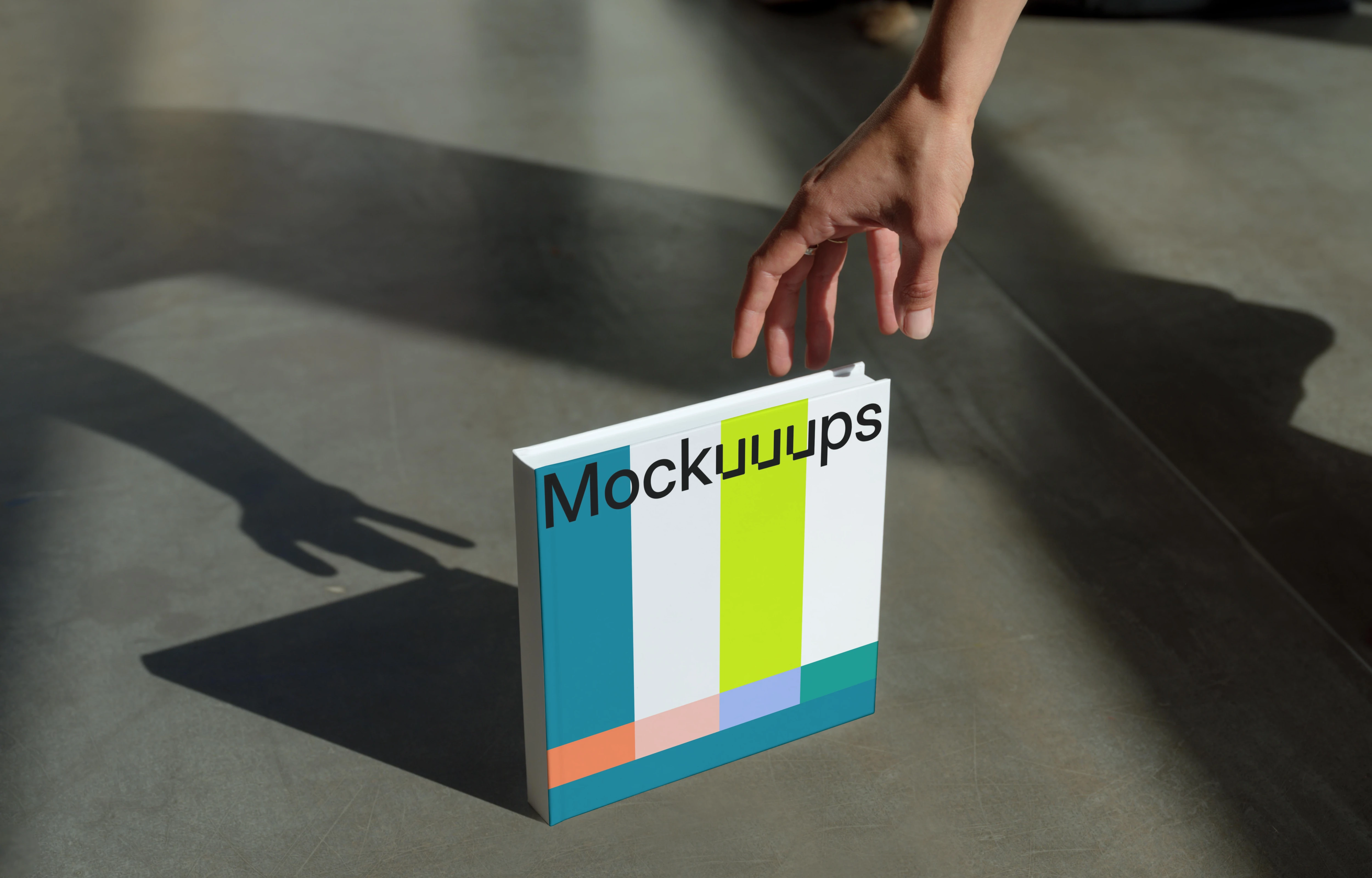 Mockup of a square book on a concrete surface with a hand reaching