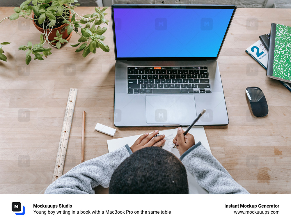 Young boy writing in a book with a MacBook Pro on the same table