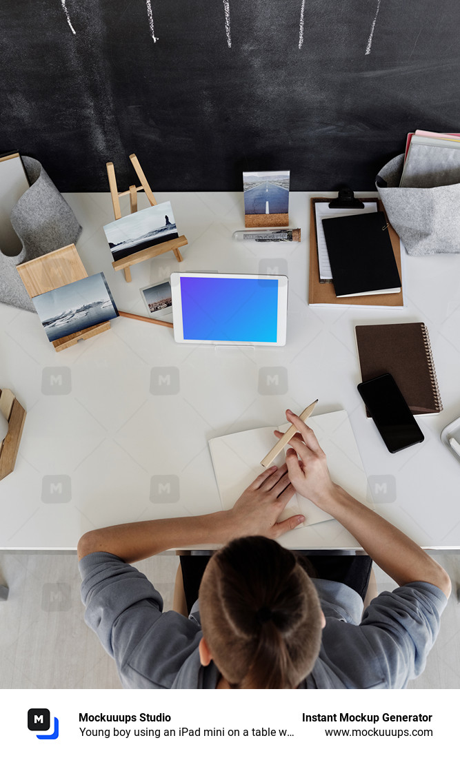 Young boy using an iPad mini on a table with a jotter by the side mockup