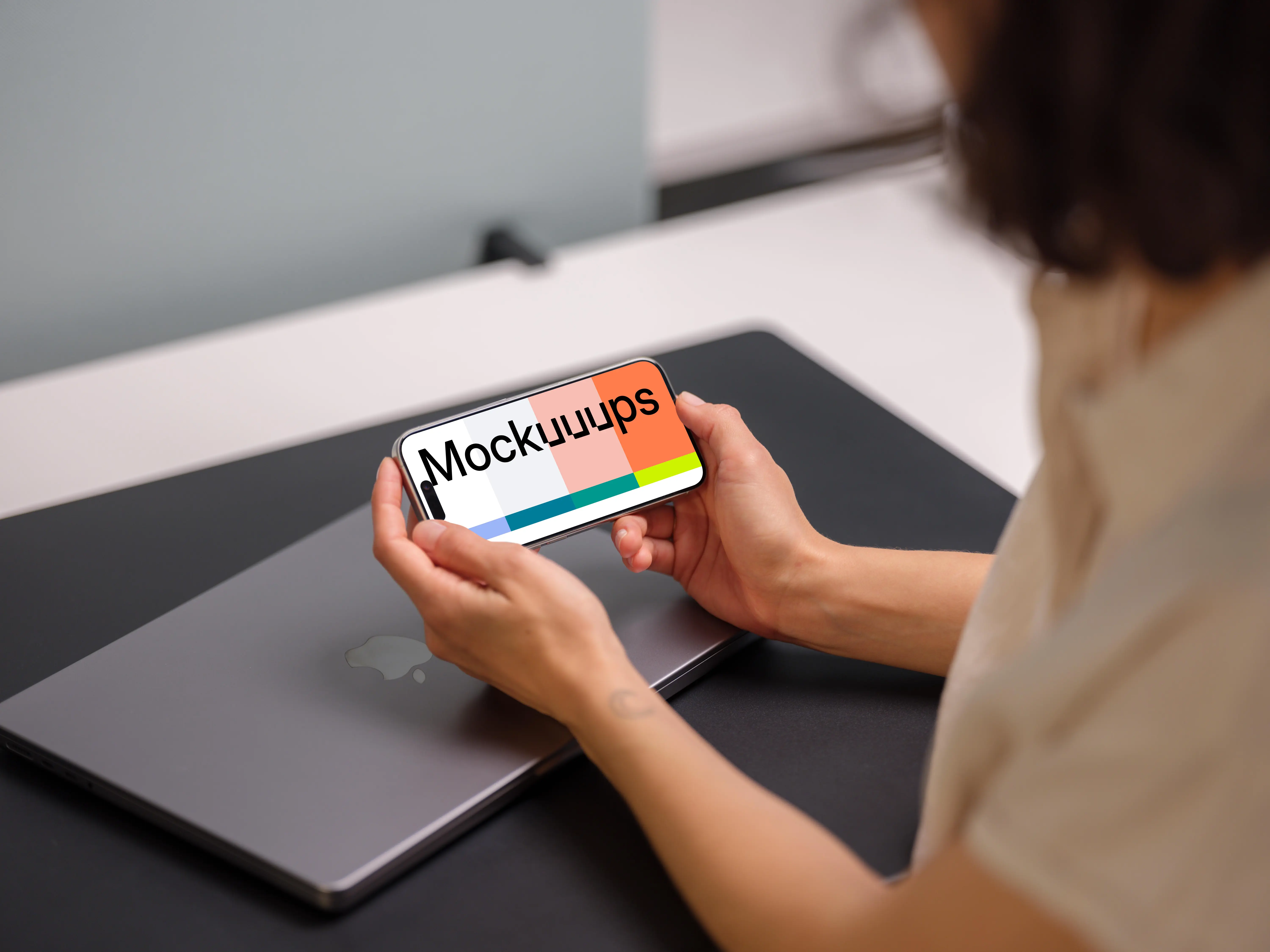 iPhone 15 Pro mockup in a woman's hand over a laptop