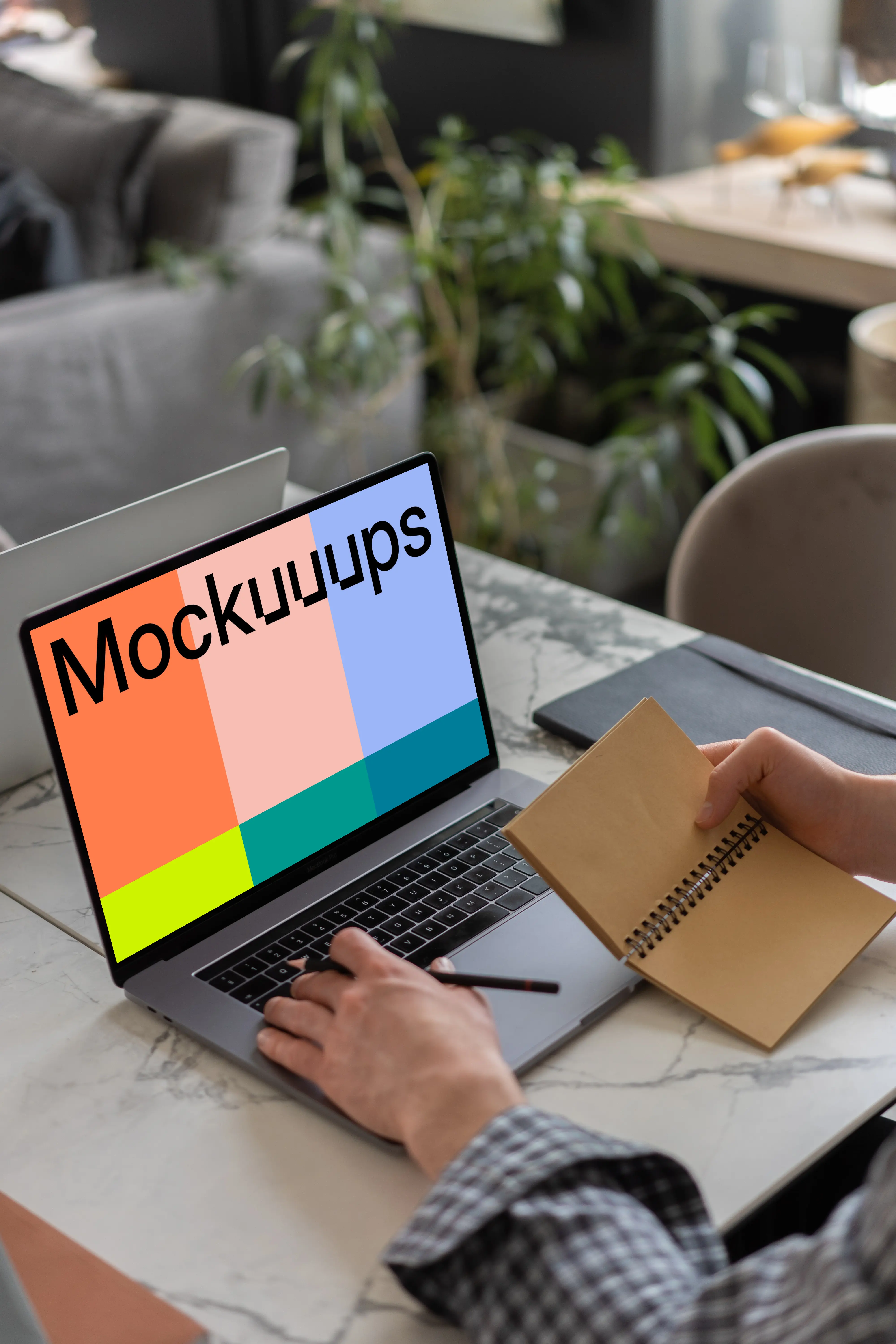 MacBook Pro mockup on a table with a jotter held beside it