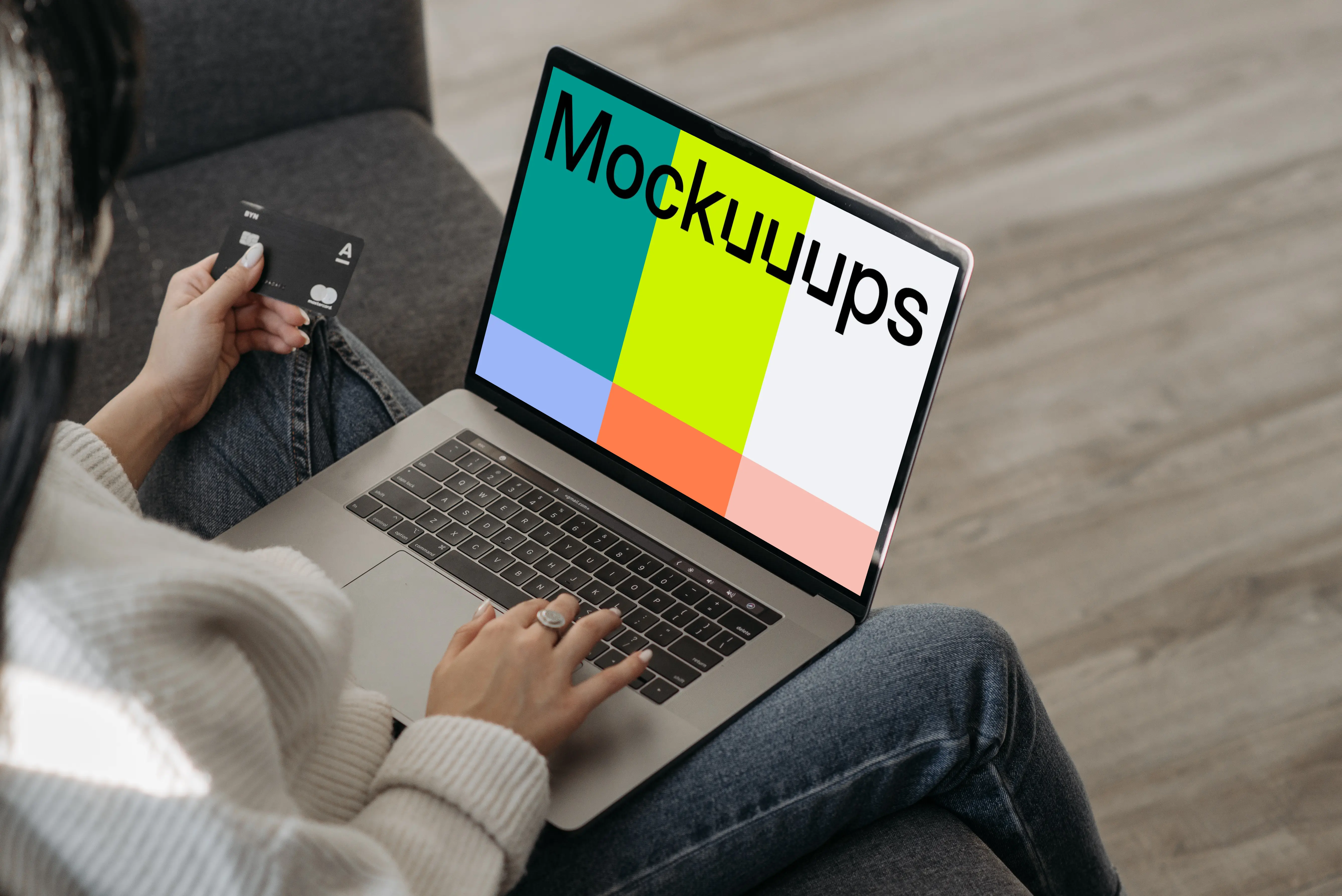 Mockup of female user on a couch shopping online with her grey MacBook and a MasterCard in hand