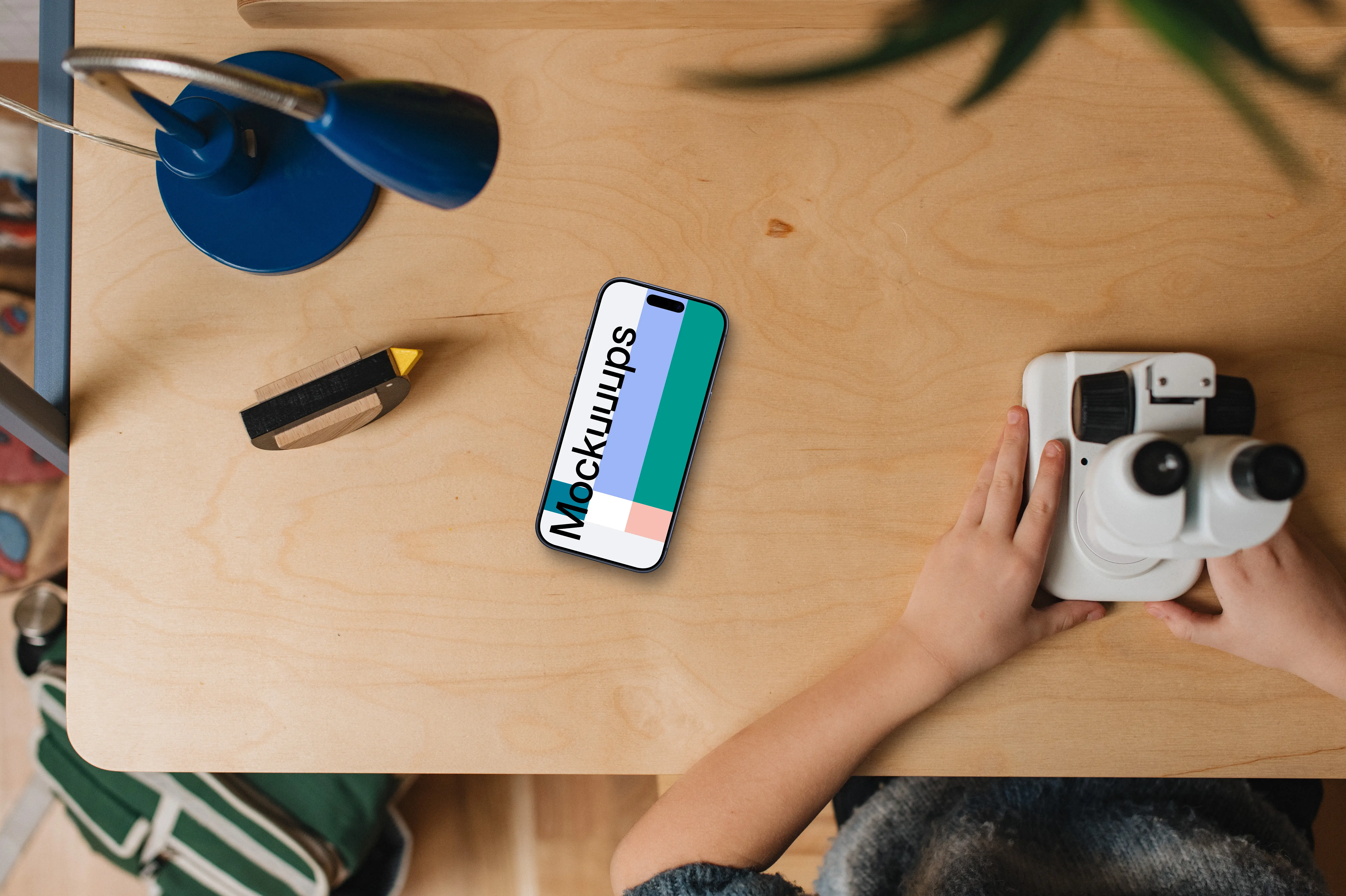 Smartphone mockup on wooden desk with kids' hands and toys