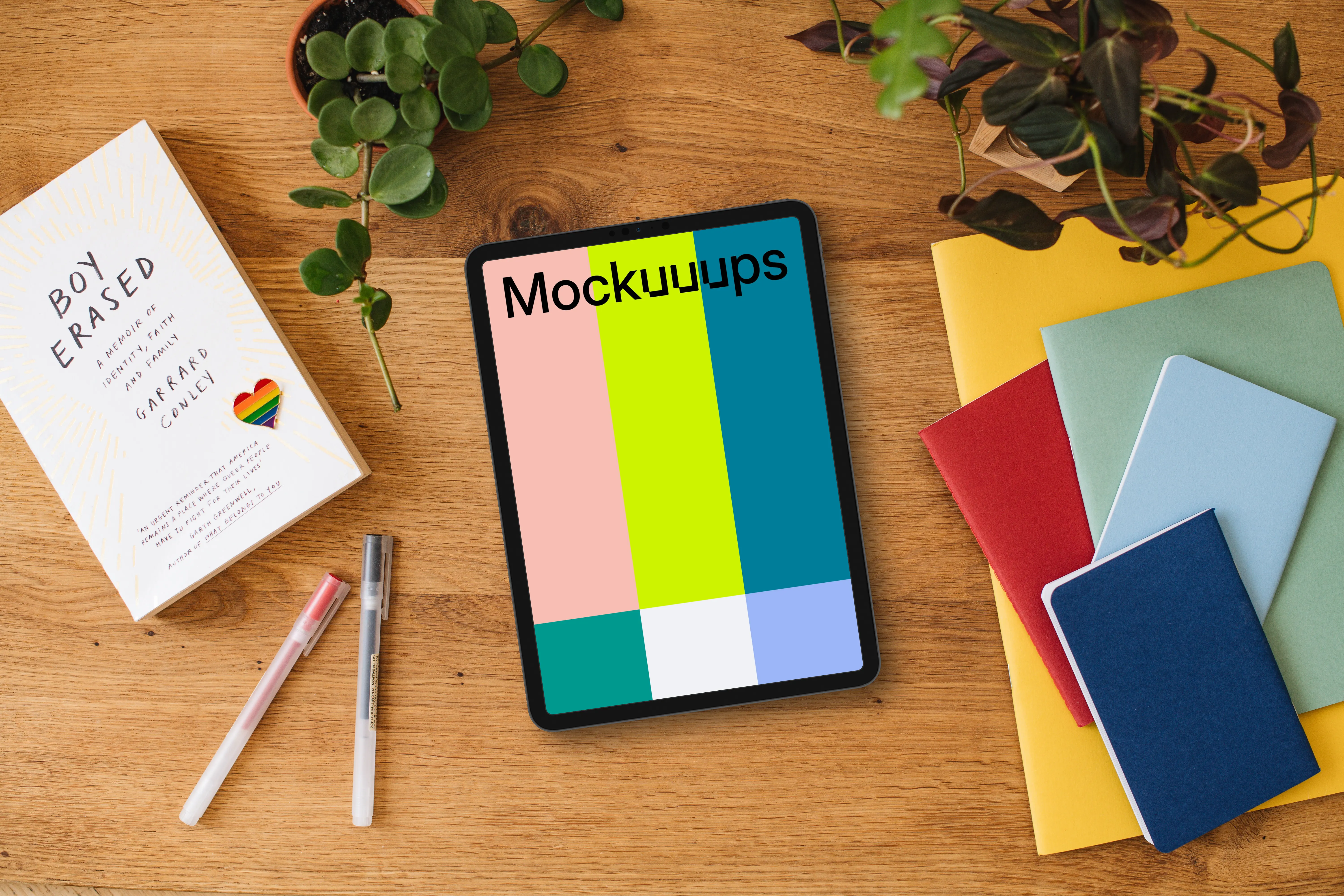 Tablet mockup on a wooden desk with pride enamel pin and colorful notebooks
