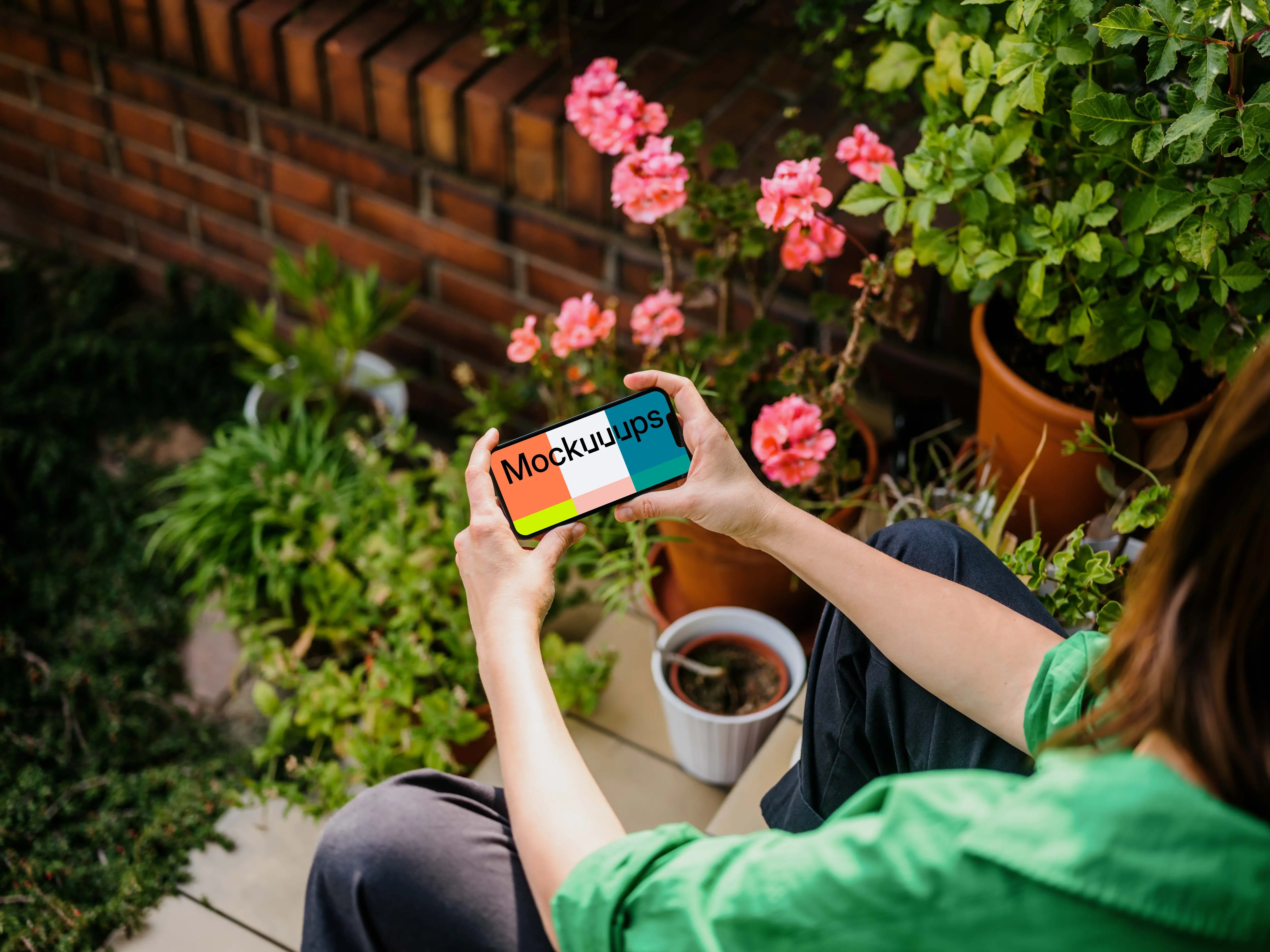 Woman sitting in garden while holding an iPhone 13 mockup