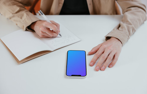 iPhone mockup on a white table next to a notebook 