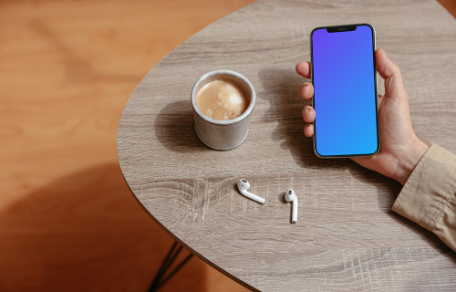 Simple handheld iPhone mockup held on the table with a pair of Airpods at the side