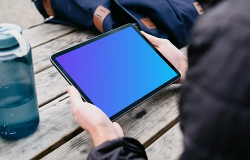 iPad Air mockup in a user’s hand with a backpack in the background