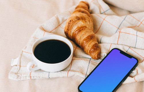 iPhone 12 Pro mockup junto a un cruasán y una taza de café