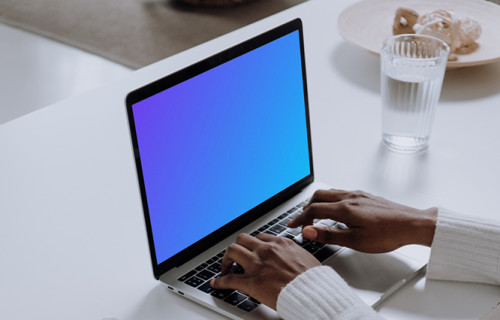 MacBook Pro Mockup on a white table with a notebook and cup of water