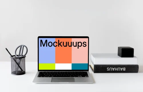 Black MacBook mockup on a white table with black textbooks at the side
