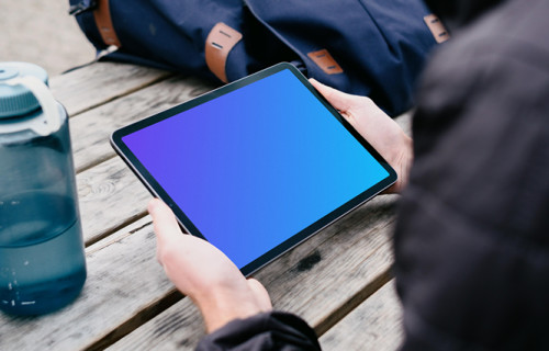 iPad Air mockup in a user’s hand with a backpack in the background
