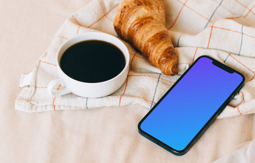 iPhone 12 Pro mockup beside a croissant and a cup of coffee