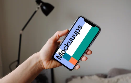 iPhone 12 Pro mockup held by user with a reading lamp in the background