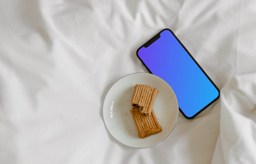 iPhone 12 Pro mockup on bed with a plate of biscuits